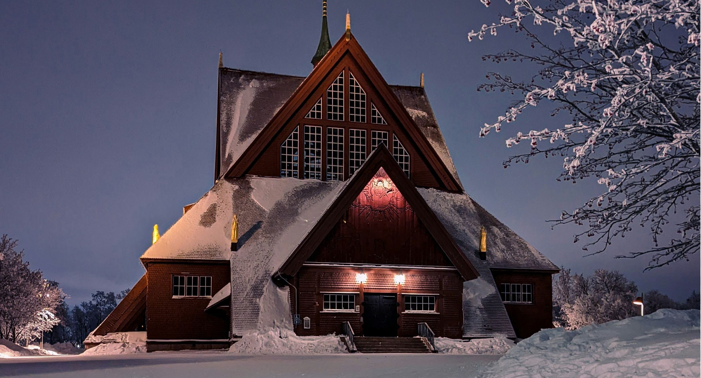 Kiruna kyrka, en stor mörkröd trékyrka, i snö i skymningen