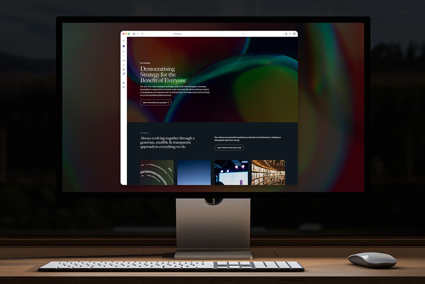 Desktop monitor on a desk showing a web page headed 'Democratising Strategy for the Benefit of Everyone'